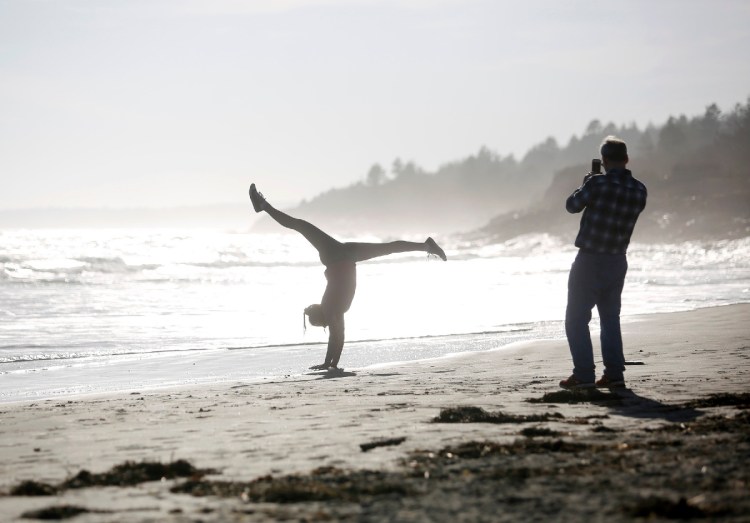Michael Malone of South Portland takes pictures of his daughter Anna, 15, as she does handstands at Higgins Beach on Wednesday, Feb. 21, 2018.The temperature reached 68 degrees on Wednesday and set a Maine record for the warmest day in February. Staff photo by Derek Davis
