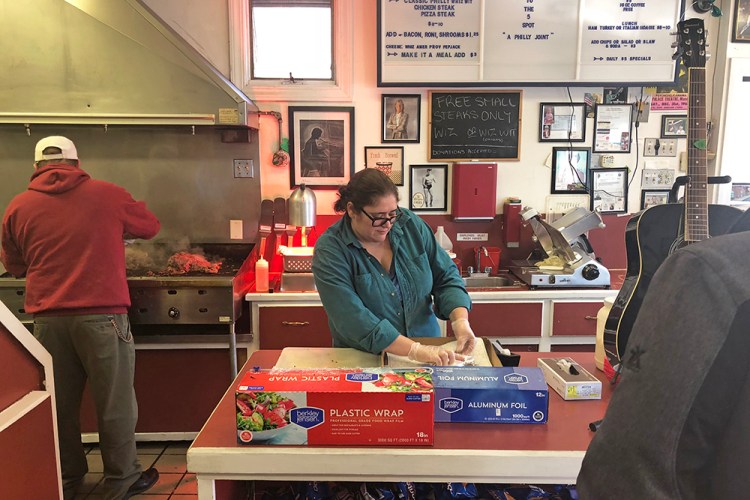 While Keith Costello slices  steak on the grill at the 5 Spot, wife and co-owner Rosetta iannaccone hands out cheesesteaks wrapped in foil Monday.

