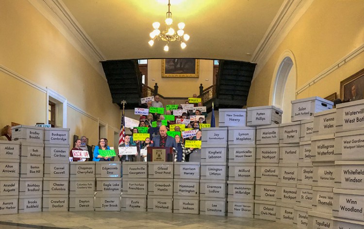Kyle Bailey stands behind 67 boxes holding over 80,000 signatures in the State House Hall of Flags in Augusta on Friday.