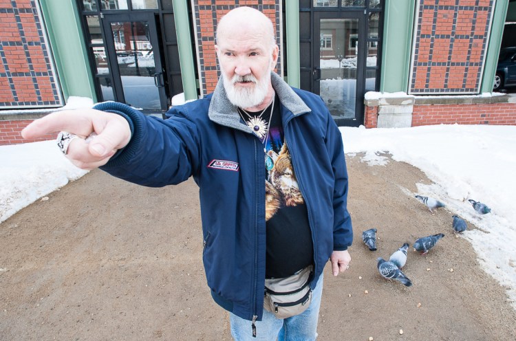 David Sites points to Oak Park Apartments in Lewiston, where he lives, as birds feed on bread he has just thrown down for them. Despite a threat of eviction for feeding the birds, Sites plans to continue feeding the pigeons, as he has done for the past 10 years. Visit sunjournal.com to watch a video of Sites feeding the birds and explaining why he plans to continue. (Russ Dillingham/Sun Journal)