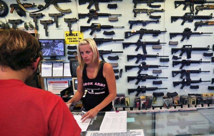 With guns displayed for sale behind her, a gun store employee helps a customer at Dragonman's, east of Colorado Springs, Colo.
