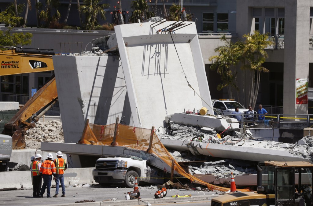 Workers stand next to a section of the collapsed pedestrian bridge Friday near Florida International University. The bridge, which was under construction, collapsed onto the busy highway Thursday, killing at least six people.