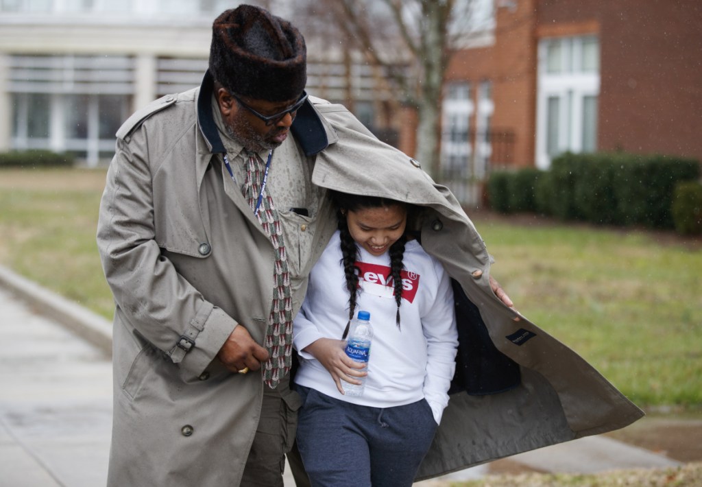 A father shelters his daughter, a student from Great Mills High School, from the rain as he picks her up from Leonardtown High School in Leonardtown, Md., on Tuesday after Great Mills was evacuated.