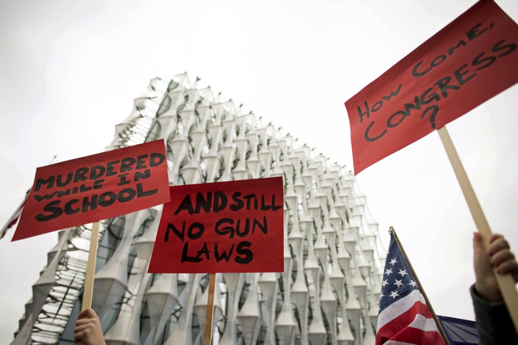 Protesters hold up signs outside the US Embassy in London, Saturday March 24, 2018,  in solidarity with the "March for Our Lives" protest against gun violence. (Stefan Rousseau/PA via AP)