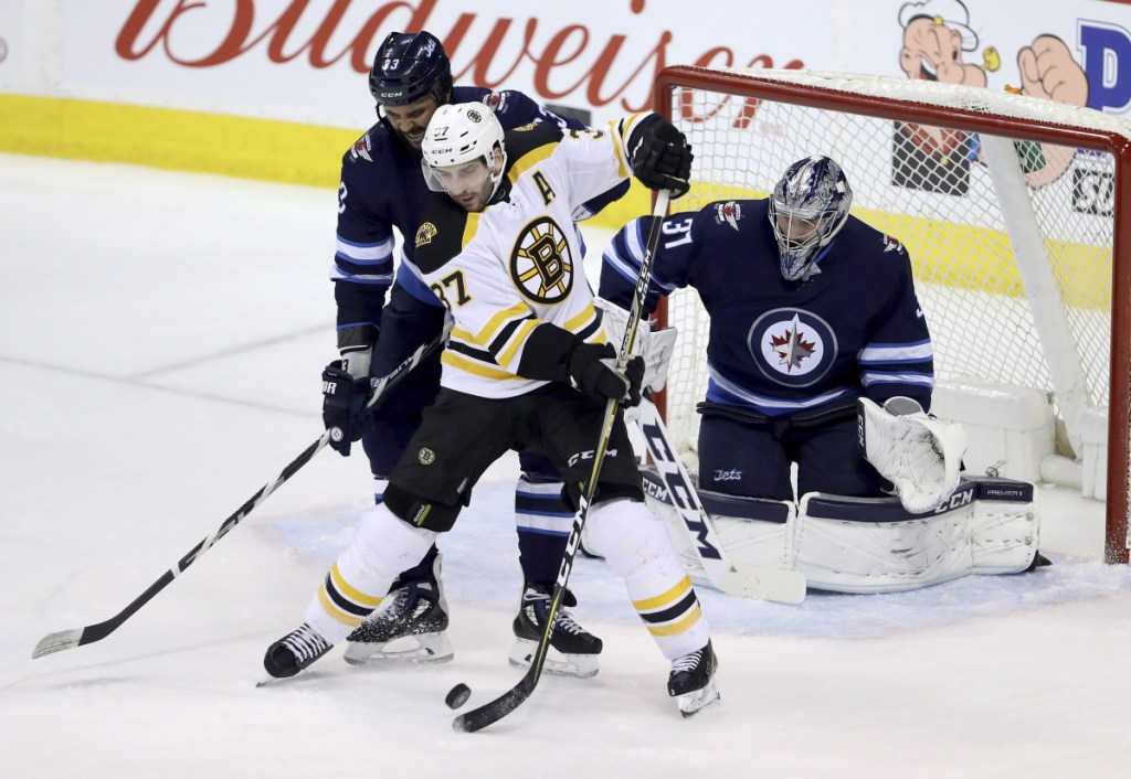 Boston's Patrice Bergeron, center, deflects a shot as Winnipeg goaltender Connor Hellebuyck, right, and Dustin Byfuglien converge during Tuesday's game in Winnipeg.