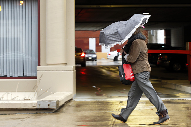 A woman walking against strong wind gusts on Middle Street takes what shelter she can under a collapsing umbrella Friday morning.
