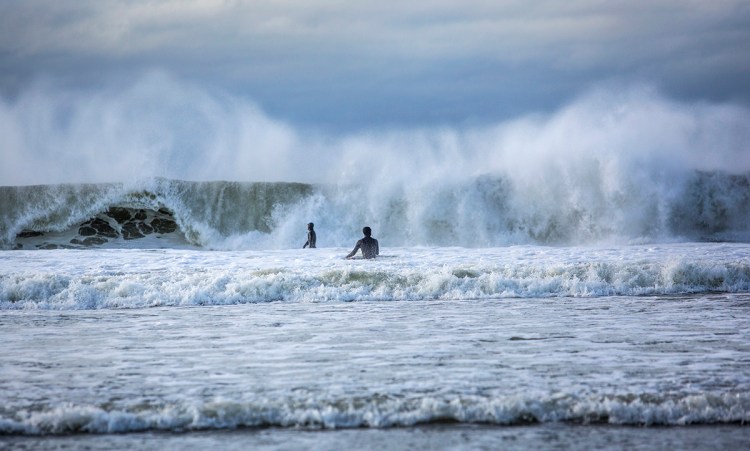 Surfers wade into heavy surf while making their way out to a break at Higgins Beach on March 5 in Scarborough.