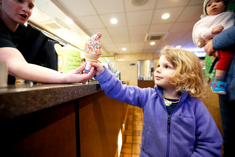 Kendra Laughlin, manager of a Dairy Queen store on Main Street in Westbrook, hands a free small ice cream cone to Emilia Lovejoy, 3, of Portland, while sister Madeline, 1, looks on. The franchise location was offering free cones to celebrate the first day of spring.