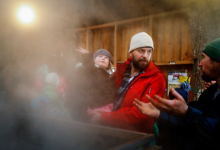 Linnea Miller, 3, left, runs her hand through the steam from the evaporator as her father Brent, center, speaks with Adam Parsons, right, during a tour of the sugar shack at Parsons Maple Products, March 25, 2018 in Gorham, for Maine Maple Sunday. 