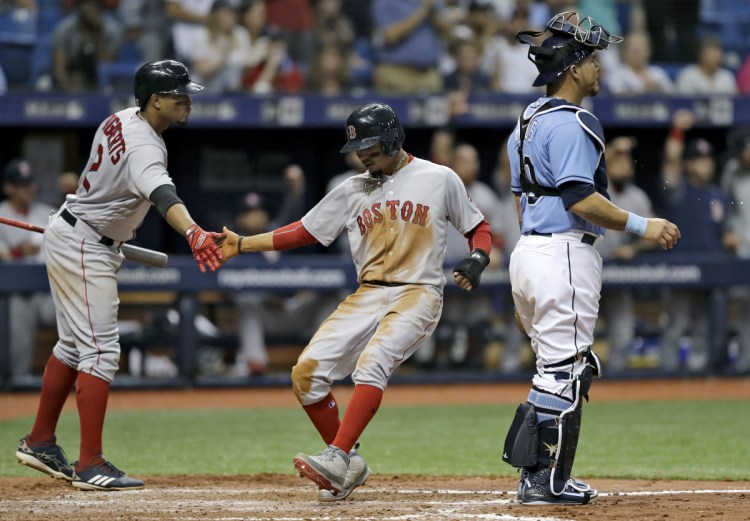 Boston's Mookie Betts, center, slaps hands with on-deck batter Xander Bogaerts, left, after scoring past Tampa Bay Rays catcher Wilson Ramos on an RBI single by J.D. Martinez in the fifth inning of a the Red Sox' 2-1 win Sunday in St. Petersburg, Florida.