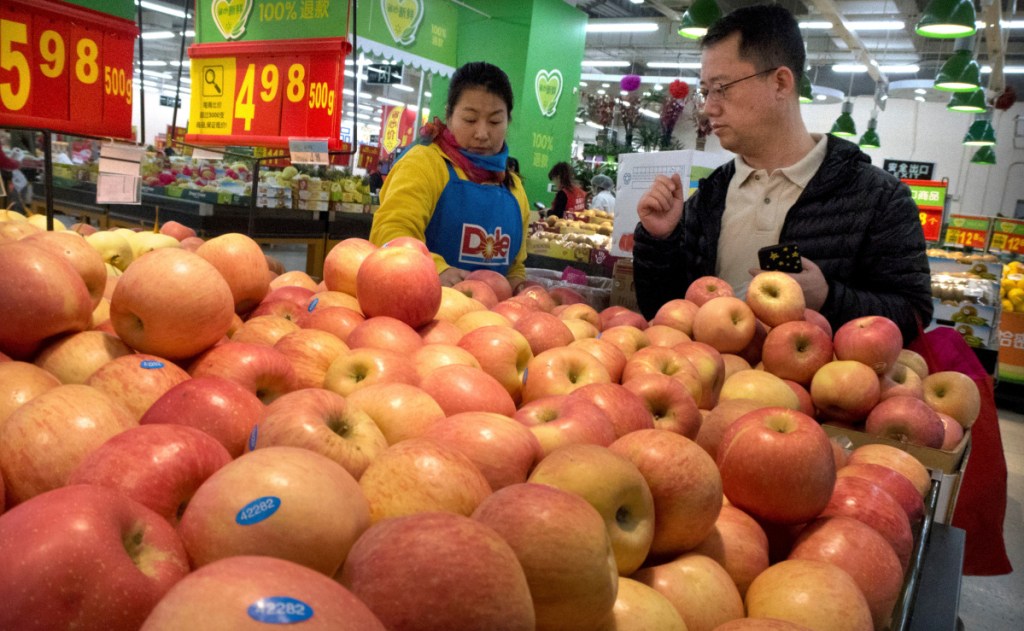 A woman wearing a uniform with the logo of an American produce company helps a customer shop for apples in a supermarket in Beijing. China raised import duties on a $3 billion list of U.S. pork, fruit and other products Monday.
