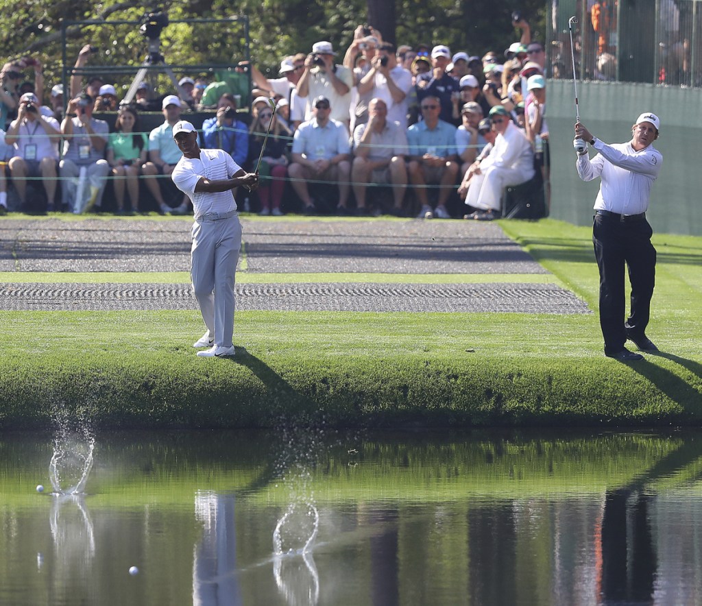 Tiger Woods, left, and Phil Mickelson skip their shots across the pond to the 16th green while clowning around for the crowd during a practice round at Augusta National Golf Club on Tuesday.