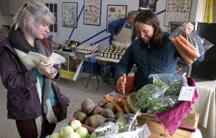 Tesse Rau of Augusta, left, buys carrots Tuesday from farmer Dalziel Lewis of China at the farmers market in Augusta. 