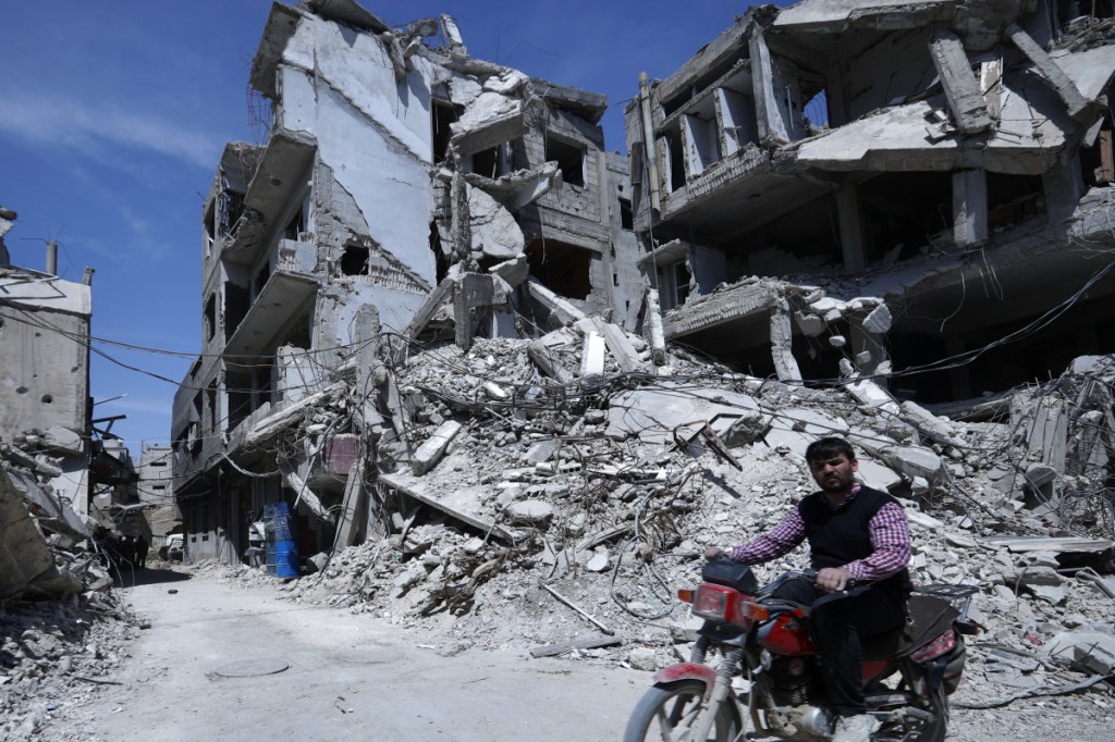 A man rides past destruction in the town of Douma, the site of a suspected chemical weapons attack, near Damascus, Syria, Monday, April 16, 2018. Faisal Mekdad, Syria's deputy foreign minister, said on Monday that his country is "fully ready" to cooperate with the fact-finding mission from the Organization for the Prohibition of Chemical Weapons that's in Syria to investigate the alleged chemical attack that triggered U.S.-led airstrikes. (AP Photo/Hassan Ammar)