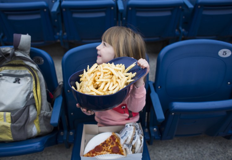 Portland restaurateurs Andrew and Briana Volk's daughter, Oona, holds a helmet full of fries at the Sea Dogs' home opener Friday.