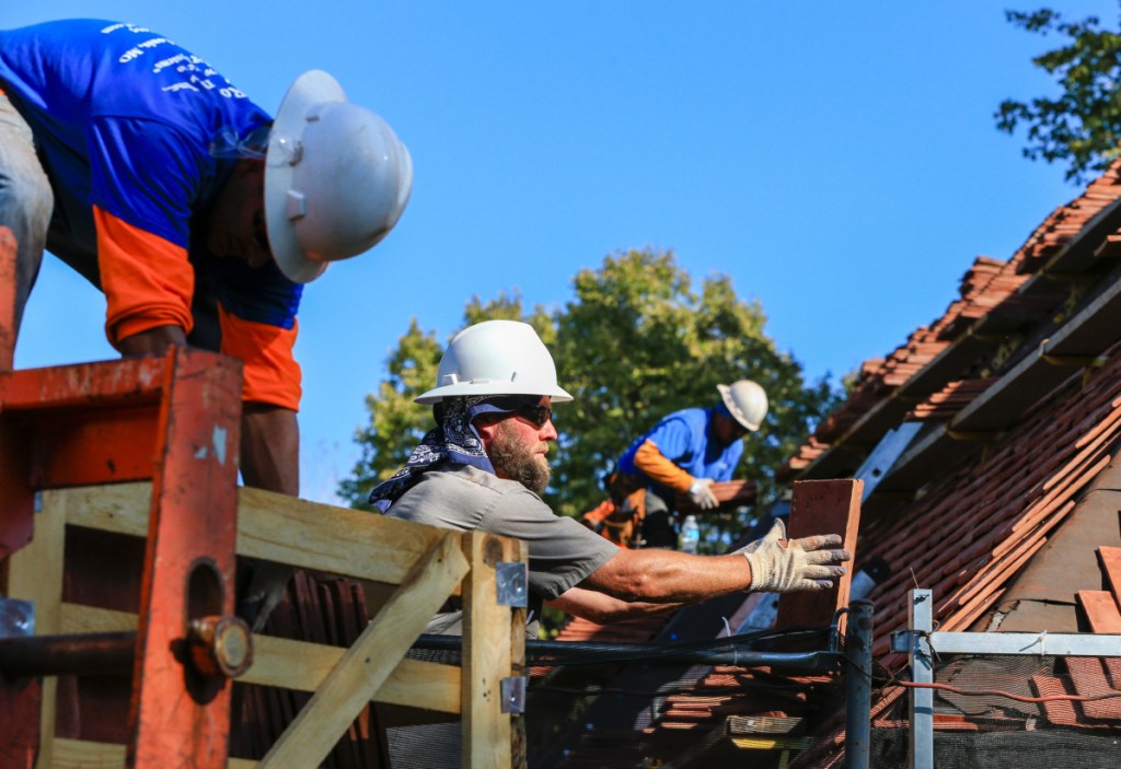 In this photo from 2015, construction workers lay tiles on the roof of a house in Boys Town, Neb. Repairing hail-damaged roofs in the village that sheltered at-risk youth since the 1930s is expensive because the campus is considered a national landmark with a look that has to be preserved. The repairs were financed with the help of the Nebraska Job Creation and Mainstreet Revitalization Act, a new state tax credit designed to revive historic buildings. (AP Photo/Nati Harnik)