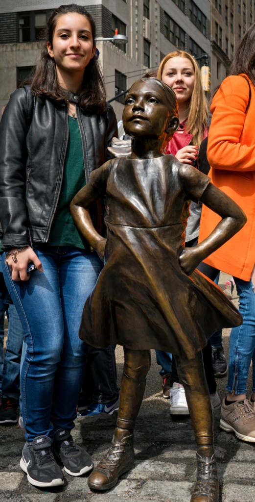 Two girls pose for photos with the "Fearless Girl" sculpture in lower Manhattan, New York.