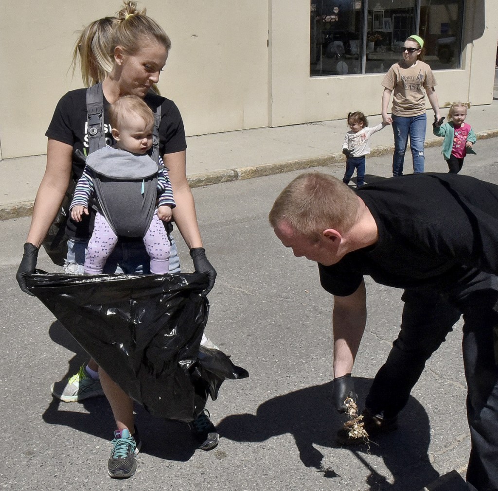 Molly Bofia with her daughter Isla Blue in a pack hold open a bag for Brian Clunie who along with others picked up litter near the Concourse in Waterville as part of the Earth Day celebration on Sunday.