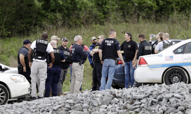 Police gather on a road along a wooded area where Waffle House shooting suspect Travis Reinking was captured Monday in Nashville, Tenn. His father, who returned his son's guns to him after they were seized by law enforcement, could face charges.