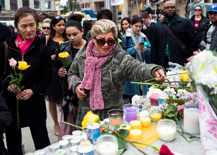 Ozra Kenari, center, places flowers as she cries at a memorial for the victims along Yonge Street the day after a driver drove a van down sidewalks, striking pedestrians in his path, in Toronto, Tuesday