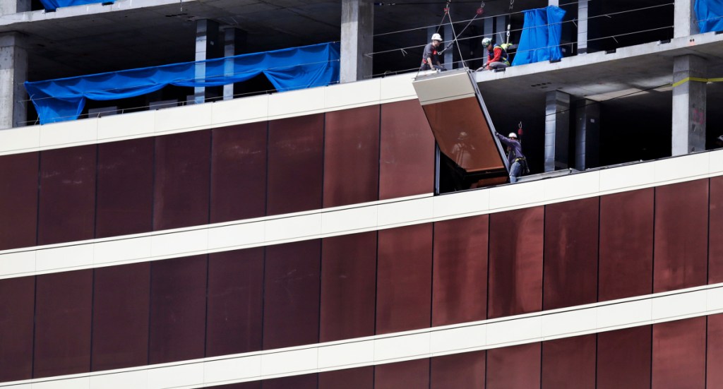 Construction workers install glass panels on the facade at the Wynn Resorts casino site in Everett, Mass., Thursday.