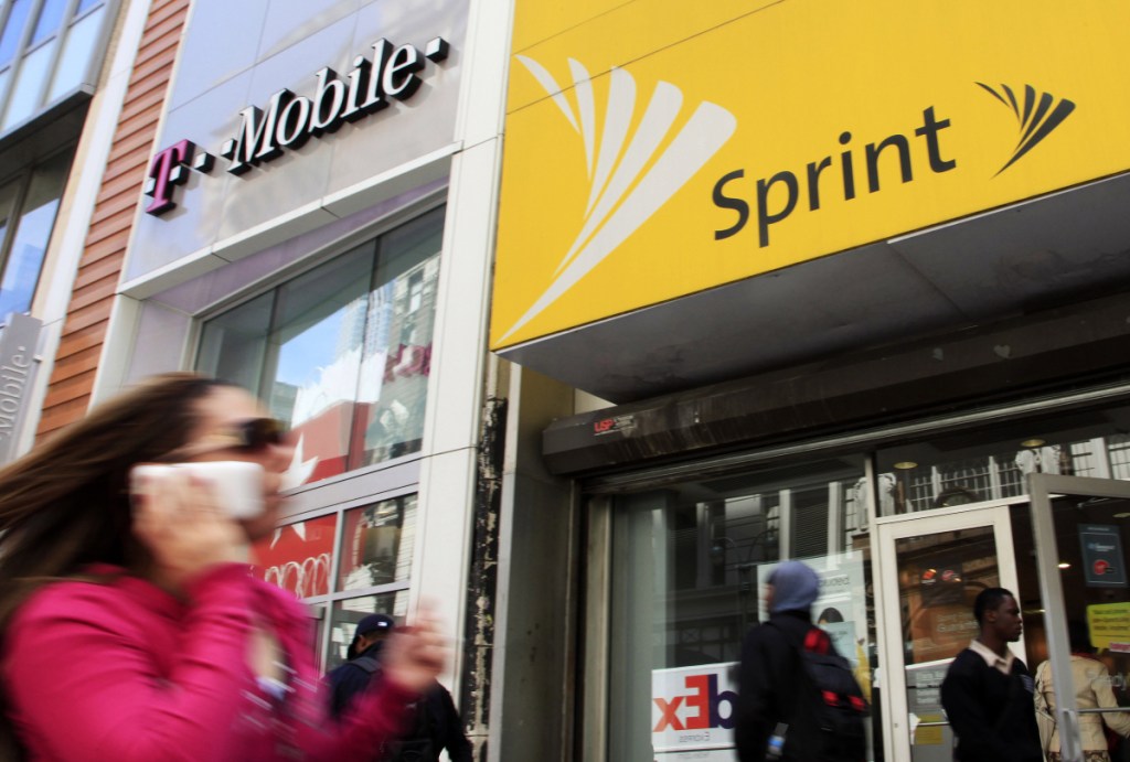 A woman using a cell phone walks past T-Mobile and Sprint stores in New York. The two companies announced a roughly $26.8 billion merger on Sunday.