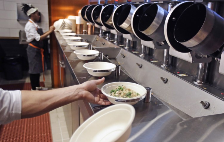 A worker lifts a lunch bowl off the production line at Spyce, a restaurant that uses an automated cooking process, after the eatery opened Thursday in Boston. Despite the high-tech machinery, the restaurant still employs plenty of humans.