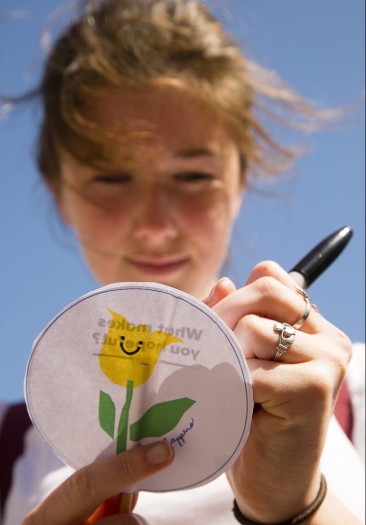 Anna Friberg, 18, of Cape Elizabeth writes a message on a paper marker as part of the Yellow Tulip Project last May 7 in Portland's Lincoln Park. Sunday's gathering is meant to be a time for celebration, with hope for those who are struggling.