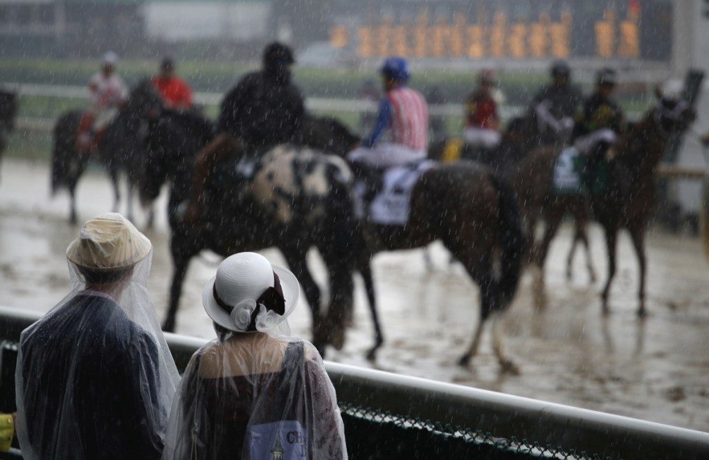 Fans watch race horses as they walk on the track through heavy rain before the 144th running of the Kentucky Derby horse race at Churchill Downs Saturday in Louisville, Ky.