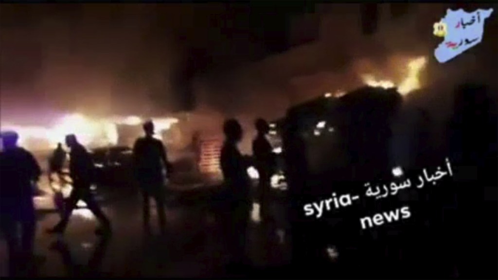 This image from video shows people standing in front of flames rising after an attack on an area known to have numerous Syrian army military bases, in Kisweh, south of Damascus, Syria, on Tuesday. In return, Iranian forces based in Syria fired 20 rockets at Israeli front-line military positions in the Golan Heights early Thursday.
