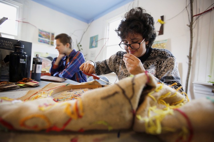 Lidia Woofenden, 21, right, joined by art mentor Julianne Carle, works on a needlepoint design at Spindleworks, a Brunswick arts and crafts studio for adults with intellectual disabilities. A cut in reimbursement rates for MaineCare, effective July 1, has created a looming crisis for group homes as well as day programs like these.