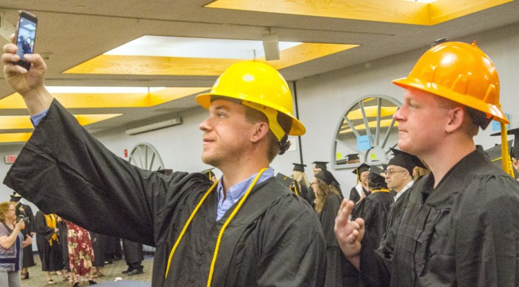 Erik Anderson, left, snaps a selfie Saturday with fellow electrical lineworker technology graduate Seth Blanchard before the KVCC graduation at the Augusta Civic Center.