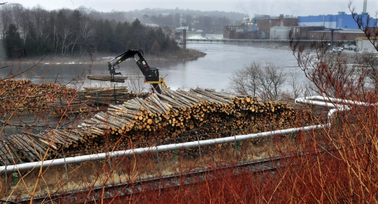 A worker unloads logs in a wood yard in 2016. The logs would be used to make paper at the Madison Paper Industries mill, in the background.