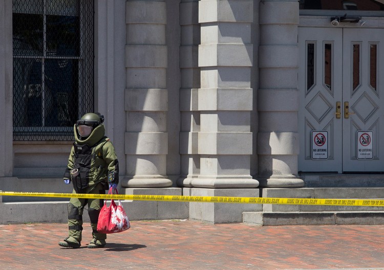 A bomb squad technician removes a suspicious bag after X-raying it on Wednesday in the Old Port. The bag was left on the corner of Pearl and Commercial streets, in front of the U.S. Custom House. 
