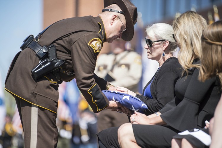 Somerset County Sheriff Dale Lancaster offers a folded American flag to Sheryl Cole, widow of Cpl. Eugene Cole, during funeral services in May. The community is coming together to build a new home for Sheryl Cole.