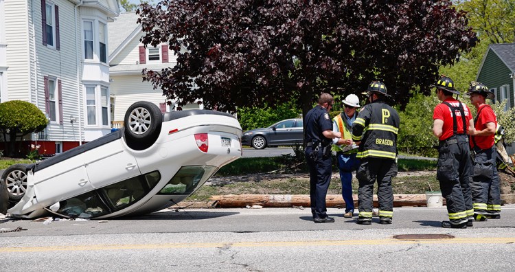 A Portland police officer consults with Portland firefighters at the scene of a car rollover on Washington Avenue early Wednesday afternoon. A snapped utility lies in the gutter in the background.