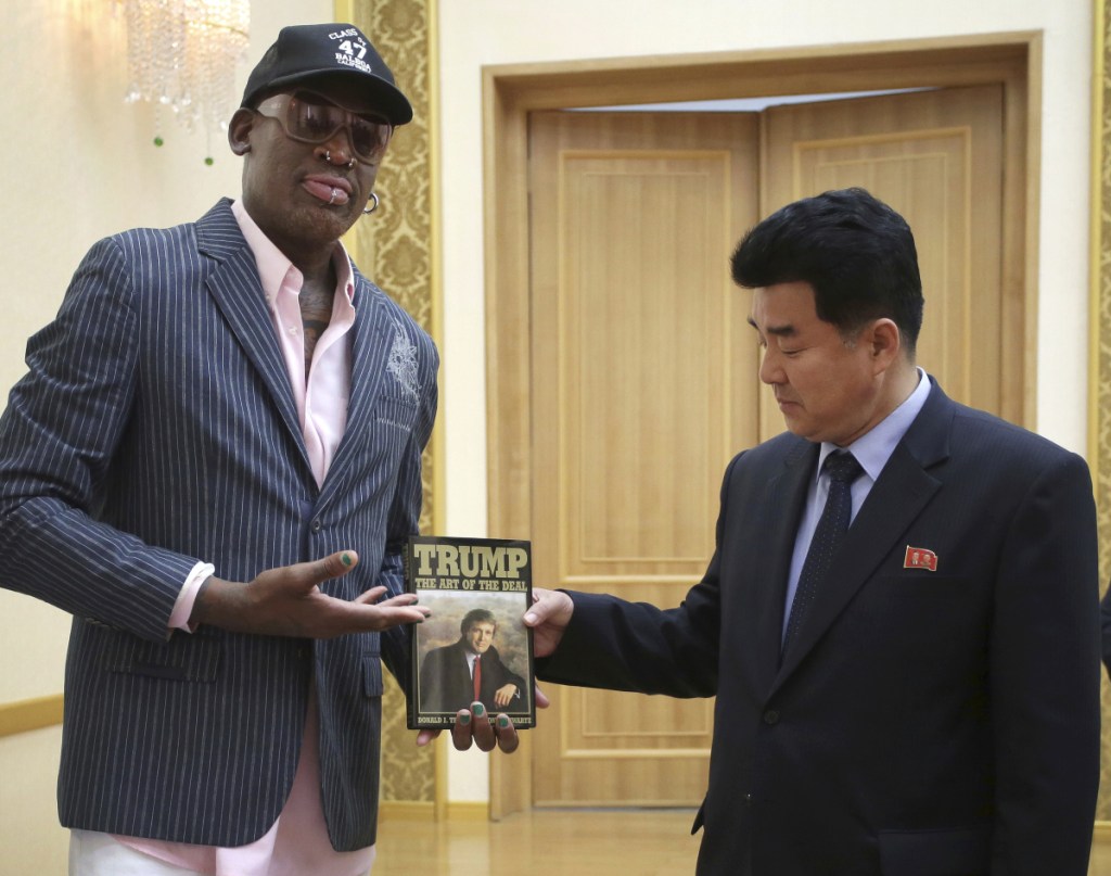 Dennis Rodman presents a book to a North Korean official in 2017. He says he'll go to Singapore for Tuesday's U.S.-North Korea summit, though President Trump said he wasn't invited.