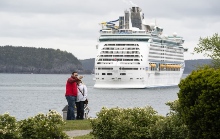 The Adventure of the Seas provides the backdrop for a couple snapping a self-portrait last week in Agamont Park along Bar Harbor's waterfront. The town expects 230,000 cruise ship passengers to visit this year and residents are struggling with how to accommodate that crush of people and the corresponding traffic snarls caused by tour buses. Residents will vote Tuesday on the purchase of a state-owned ferry terminal north of town.