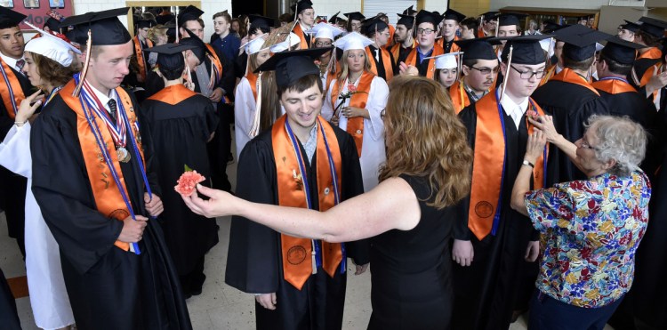 Skowhegan Area High School senior Jackman Hodges, center, gets his corsage and a hug from teacher Darcy Fitzmaurice as Eleanor McClay also pins corsages on students  prior to commencement exercises at the school Sunday.