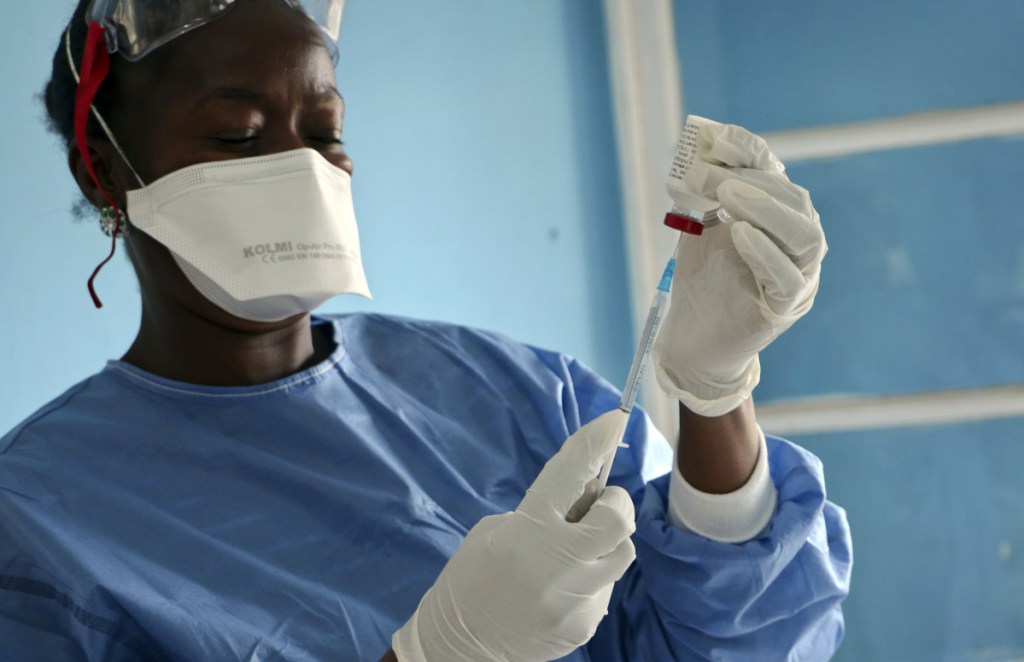 A health care worker cleans a colleague wearing Personal Protective Equipment at an Ebola treatment center in Coyah, Guinea, in 2015. At left, a World Health Organization medic prepares vaccines to give to front line aid workers, in Mbandaka, Congo, on May 30. For the first time since the Ebola virus was identified more than 40 years ago, a vaccine has been dispatched to the front lines to try to curb the current epidemic in Congo.