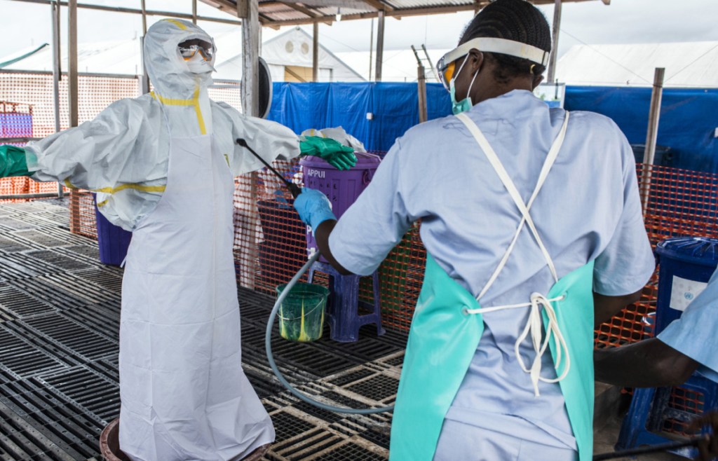 A healthcare worker cleans a colleague wearing Personal Protective Equipment at an Ebola Treatment Center in Coyah, Guinea, on Sept. 10, 2015.  MUST CREDIT: Bloomberg photo by Waldo Swiegers