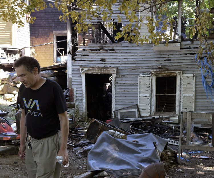 Tom Bustos walks by the burned-out remnants of his barn and home Sunday on Deane Street in Gardiner.