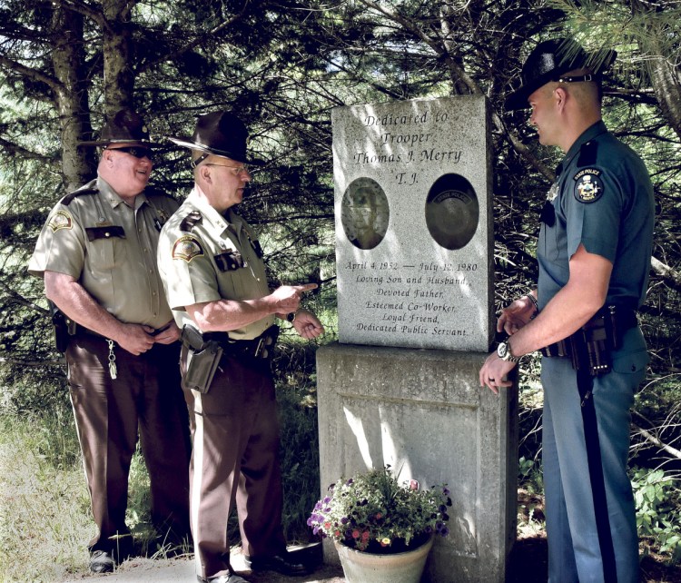 The site of the memorial to Trooper Thomas Merry, who died in the line of duty in 1980, has become obscured along the woods line on Route 2 in Palmyra. Somerset County Deputy and vice-chair of the Palmyra Board of Selectmen Mike Cray, left, Somerset County Sheriff Dale Lancaster and Trooper Eric Bronson on Thursday discuss an effort to relocate the memorial to another site nearby.