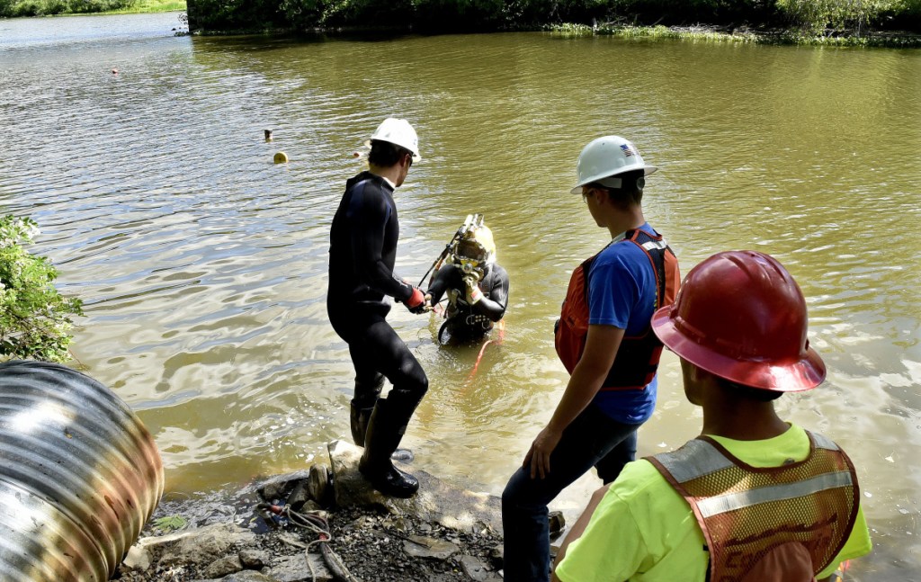 Hard-hat diver Kenny Strout, center, of Commercial Divers Inc., is handed tools to make repairs Tuesday to a 16-inch water line in Messalonskee Stream off North Riverside Drive in Waterville. The line broke Monday, stirring up sediment in the pipes and causing discoloration in the water, which nevertheless is safe to drink and use, according to the Kennebec Water District.