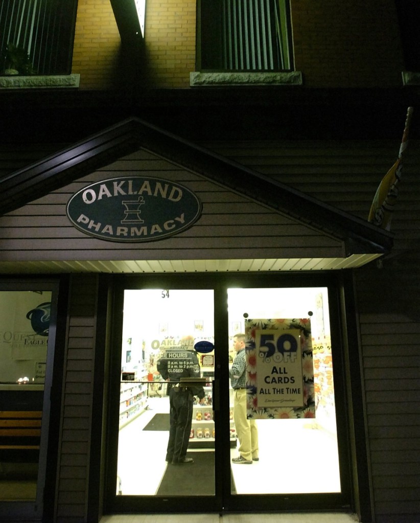 A police officer talks to an individual inside The Oakland Pharmacy on Main Street as part of the investigation of a robbery that occurred there on Oct. 31, 2007.