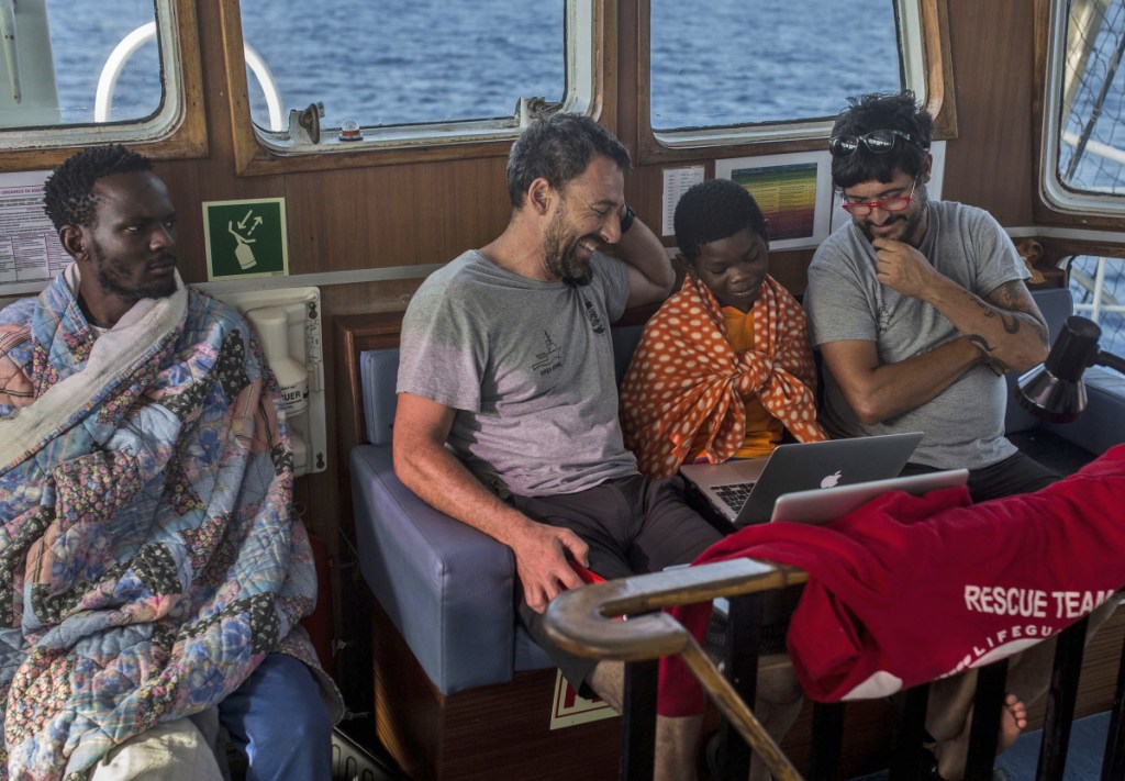 Guillermo Cañardo, chief of mission, and Marco Martinez Esteban, captain of the Open Arms boat, watch cartoons next to Khingsley Dokowada, 9, of Central African Republic, on Monday. The boat is carrying 60 migrants and will dock in Barcelona on Wednesday.
