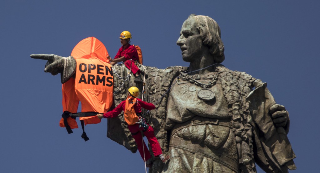Two activists climb from the Christopher Columbus statue after placing a vest with the words "Open Arms" on it in Barcelona on Wednesday,.