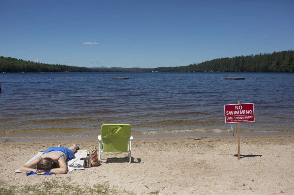 Christy Dow tans Saturday on Woods Pond Beach in Bridgton, which was closed to swimmers after some became ill. The beach reopened Tuesday after testing found the lake water to be safe.