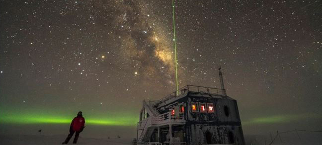 The IceCube lab lit by stars and the southern lights.