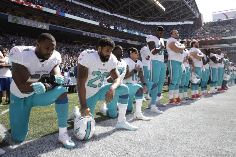 In Sept 2017, from left, Miami Dolphins' Jelani Jenkins, Arian Foster, Michael Thomas, and Kenny Stills, kneel during the singing of the national anthem before an NFL football game against the Seattle Seahawks in Seattle. Miami Dolphins players who protest on the field during the national anthem this season could be suspended for up to four games under a new team policy issued to players this week.
